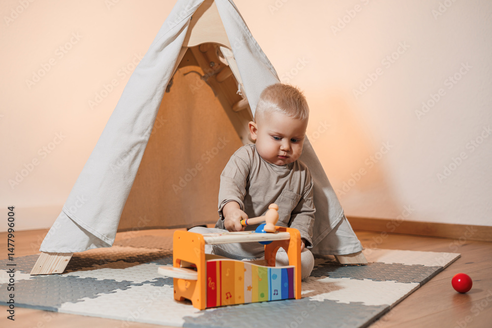 A cheerful toddler plays and creates music in a cozy, colorful tent, with a xylophone and soft playmat, fostering a vibrant atmosphere for fun learning and essential development activities