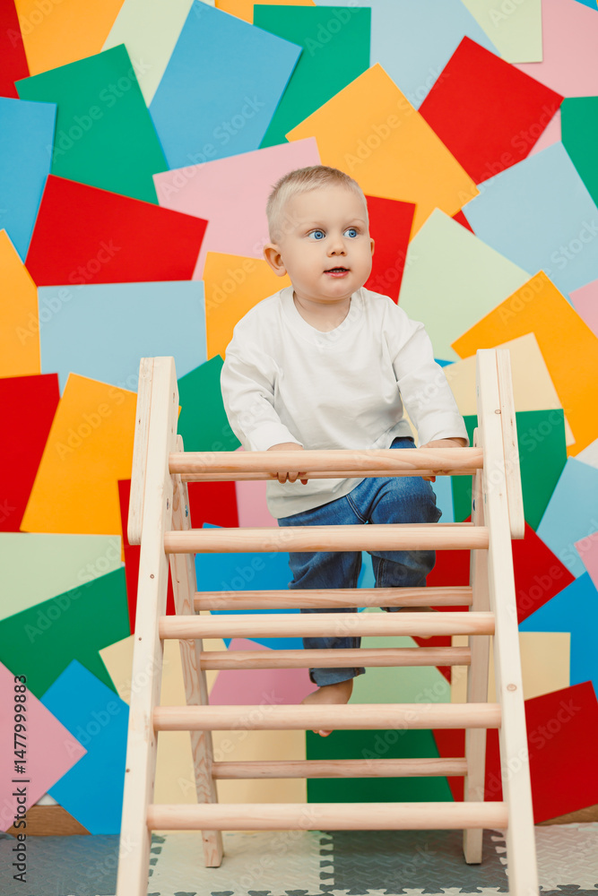 A toddler enthusiastically climbs a wooden ladder set against a vibrant backdrop filled with colorful geometric shapes, showcasing the joy of childhood exploration and adventurous play