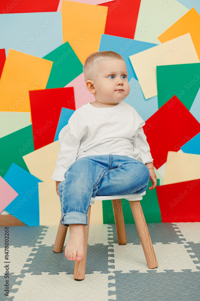 An adorable toddler sits comfortably in a chair, surrounded by a vibrant paper background, creating a delightful scene filled with joy and innocence, perfect for capturing memories