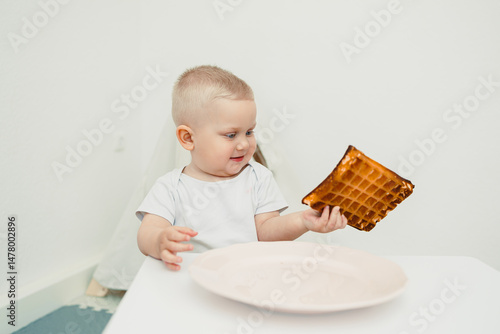Obraz na płótnie In a bright, minimalistic setting, a curious toddler joyfully explores a snack, savoring delightful experiences and creating cherished memories that embody childhood innocence and wonder w salonie
