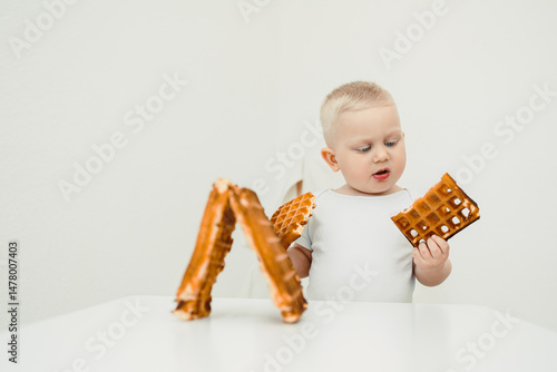 Obraz na płótnie In a bright, minimalistic setting, a curious toddler joyfully explores delightful waffle shapes, showcasing their enthusiasm and excitement during this whimsical culinary adventure w salonie