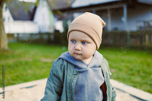 Obraz na płótnie An adorable toddler enjoying the outdoor playground setting, showcasing bright blue eyes and wearing a stylish hat, epitomizing the essence of childhood innocence and playful curiosity w salonie