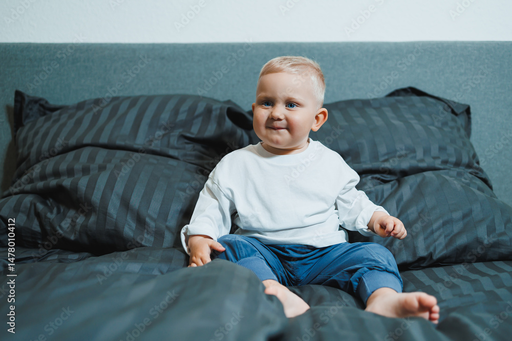 An adorable and happy toddler is sitting comfortably on a cozy bed that is surrounded by an array of soft, colorful pillows, all within a beautifully designed modern space and interior ambiance