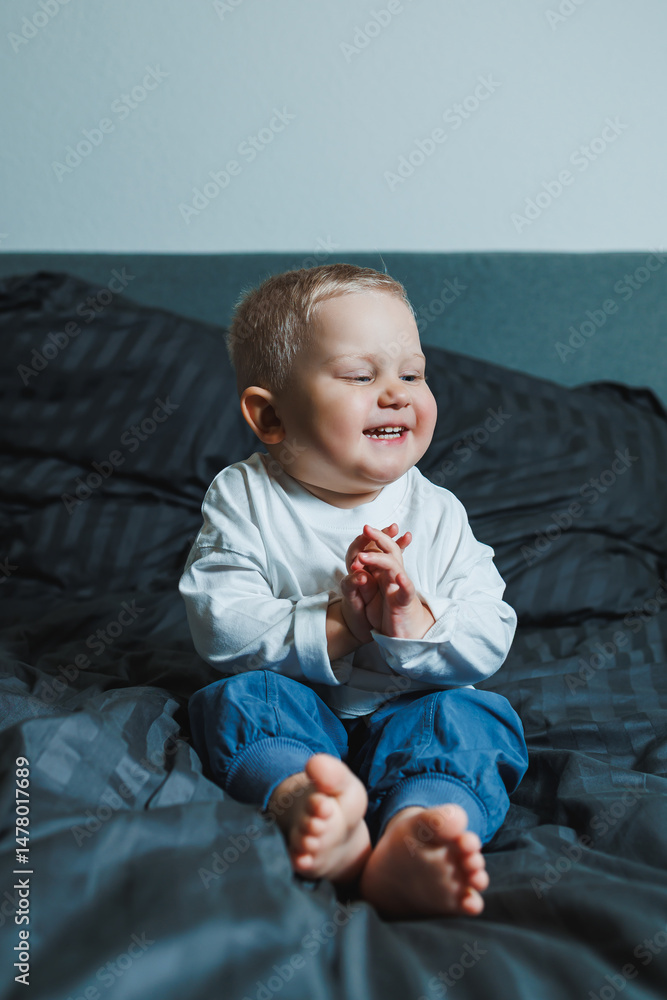 A joyful toddler sits on their cozy bed, clapping their hands with delight, creating a playful atmosphere in a warm, bright indoor space, capturing the charm of early childhood moments