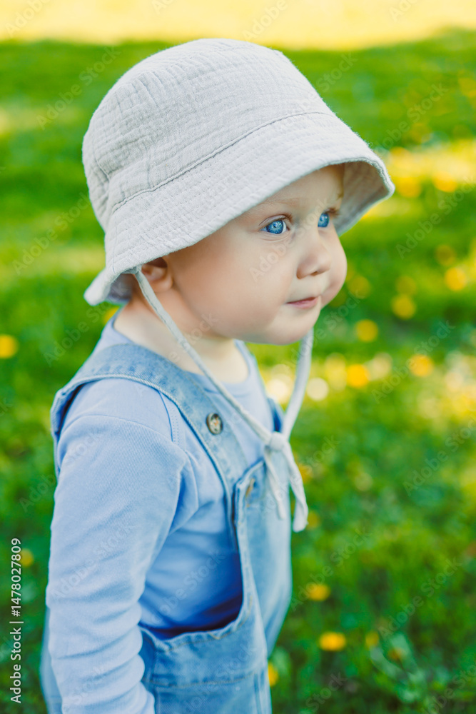 This charming child portrait shows a sweet little one in a bucket hat, joyfully exploring nature among vibrant flowers and greenery, capturing innocence and exploration beautifully
