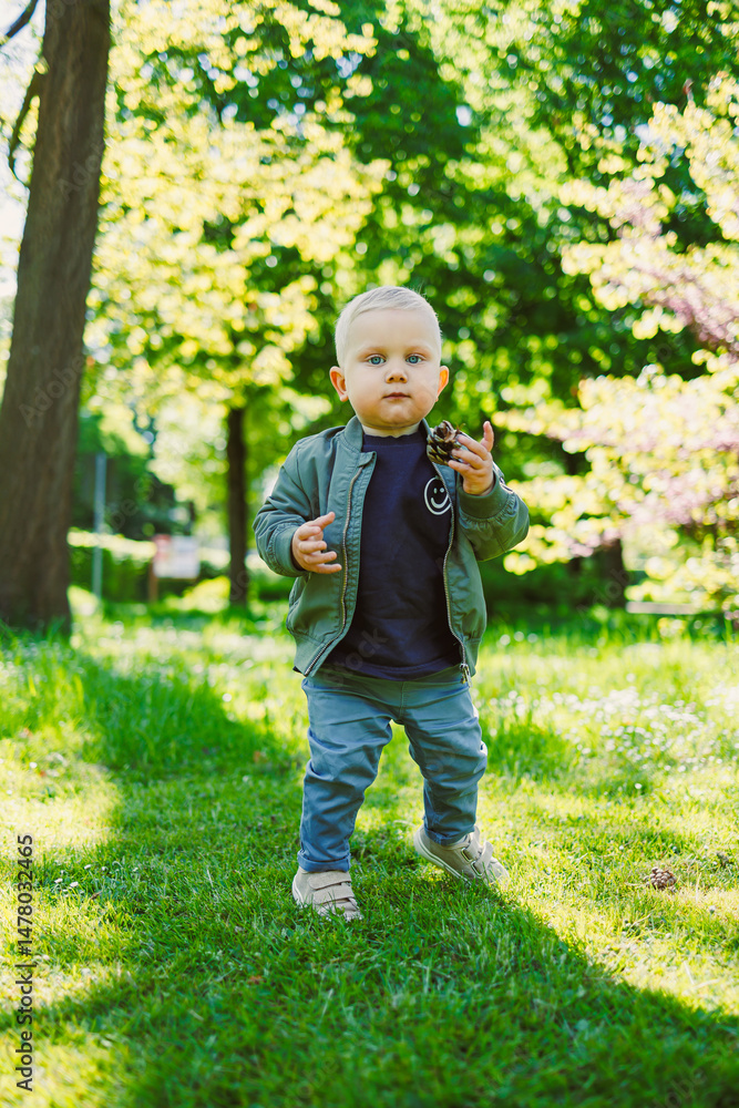 A delightful and adorable toddler is joyfully exploring the beauty of nature in a sunny, vibrant park setting, filled with greenery and the carefree essence of childhood adventure