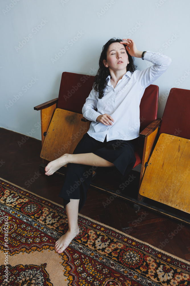 A young woman is elegantly positioned in a cozy setting, radiating an aura of serenity and showcasing her unique individuality and fashionable style amid the gentle softness of daylight streaming in