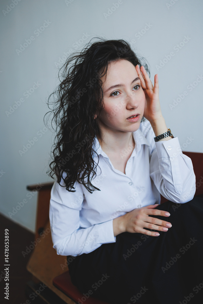 A young woman with curly hair poses in stylish attire, exuding a serene vibe that captures her chic demeanor. Her thoughtful expression adds depth, making it a captivating portrayal of modern beauty