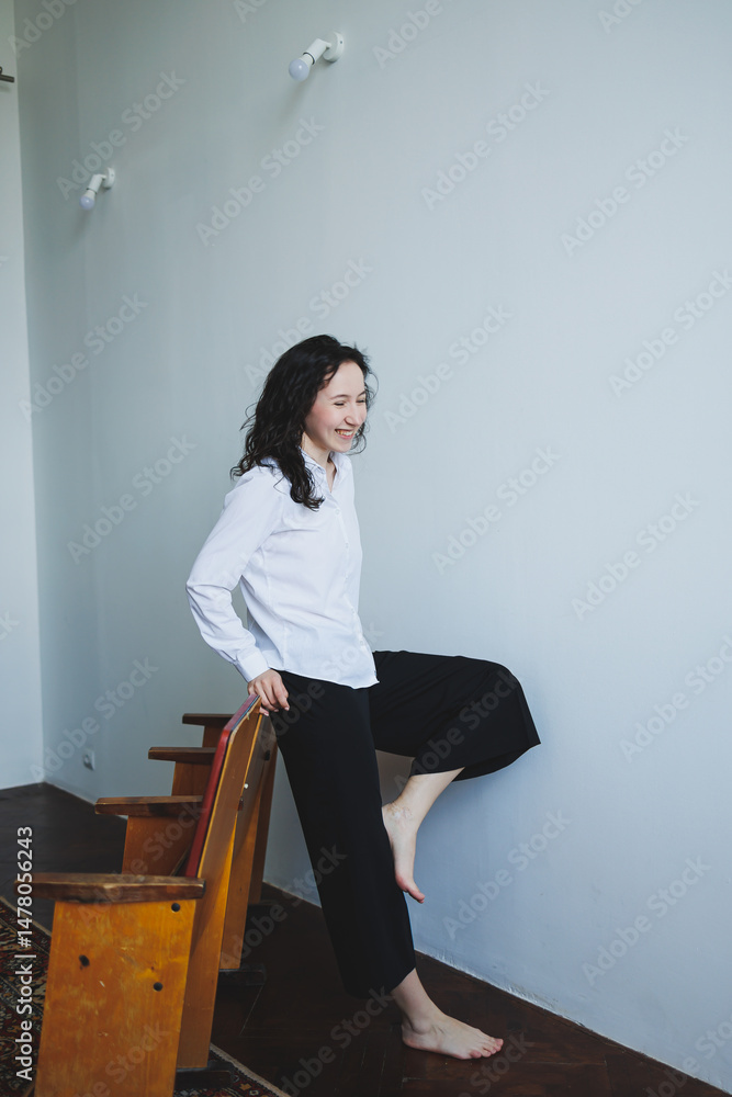 An elegant woman is playfully posing within a beautifully minimalist interior setting, exuding charm and confidence as she embraces her individuality and expresses her fashionable style