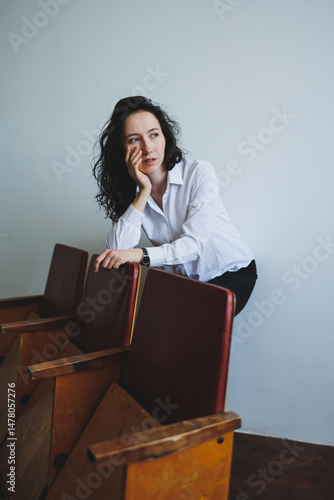 Obraz na płótnie In a stylish studio, a young woman showcases her fashion sense in a chic white shirt, posing by a vintage bench that blends modern and classic elements, creating an inspiring atmosphere w salonie