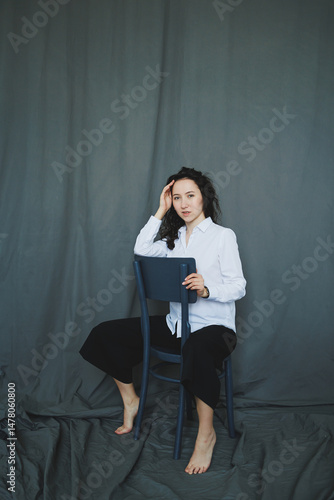 Obraz na płótnie A Contemplative Portrait Featuring a Young Woman Seated Comfortably on a Chair, Set Against a Soft Gray Backdrop, Exuding a Mood of Reflection and Introspection that Engages the Viewer Interest w salonie