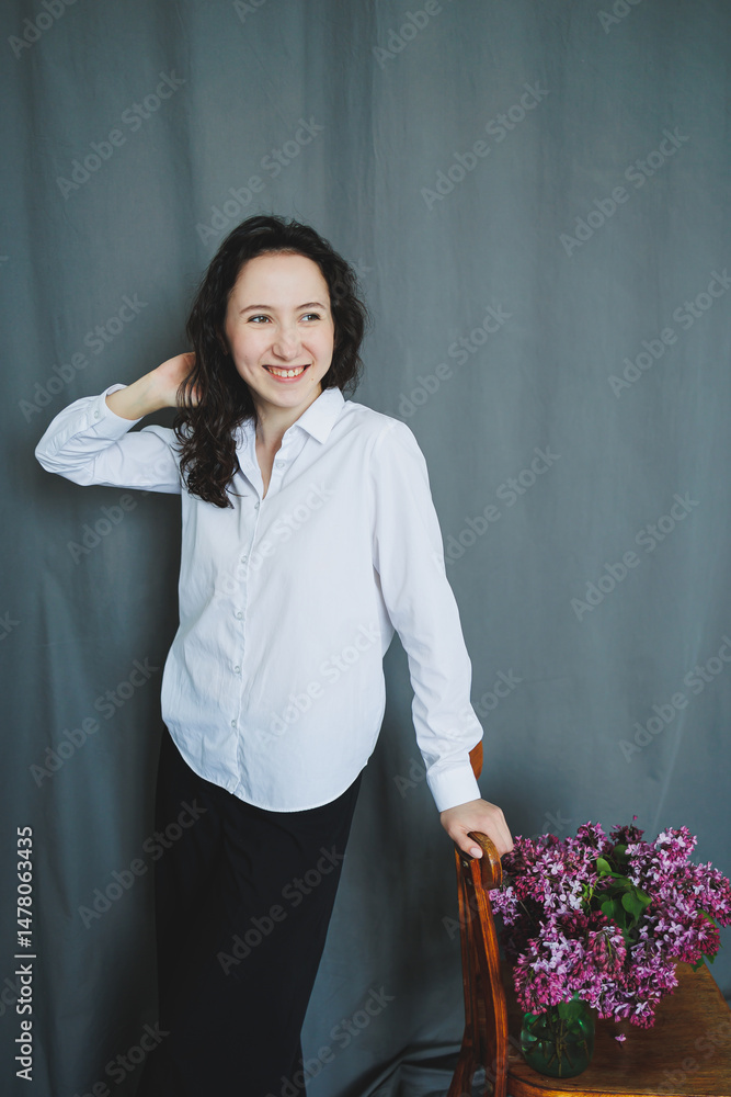 An elegant woman is gracefully posing with beautiful flowers in a modern minimalist setting that highlights her charm and beauty, creating an artistic and inspiring indoor environment