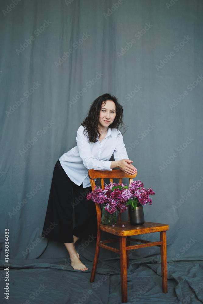 This captivating contemporary portrait shows a beautiful woman poised with vibrant flowers against a gray backdrop, merging relaxation, elegance, modern style, and the essence of nature