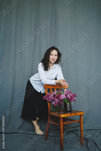 Obraz na płótnie This captivating contemporary portrait shows a beautiful woman poised with vibrant flowers against a gray backdrop, merging relaxation, elegance, modern style, and the essence of nature w salonie