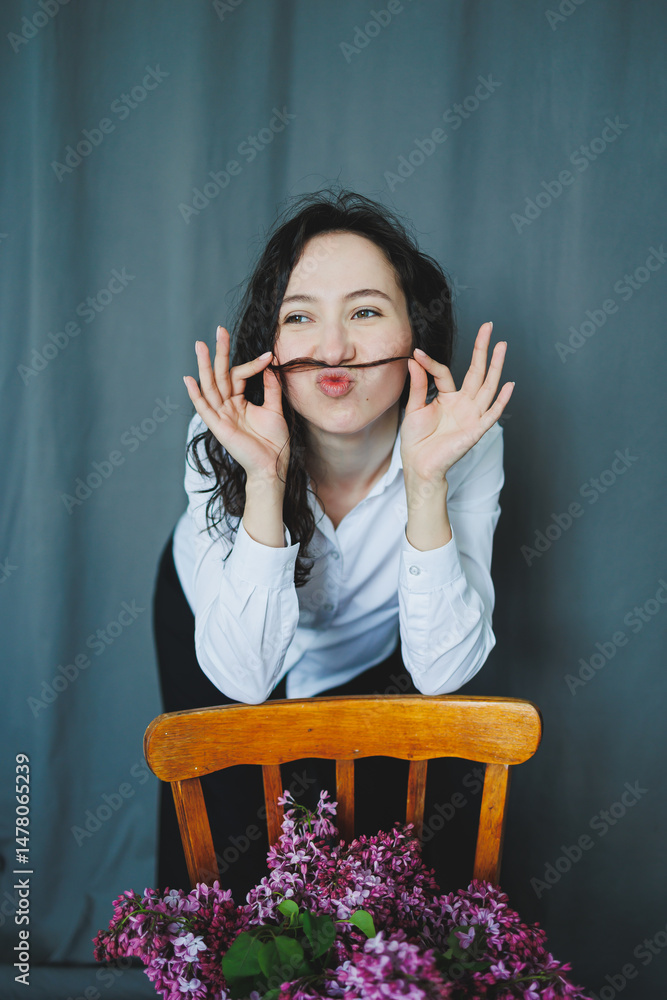 A Playful Portrait of a Young Woman Engagingly Making a Mustache Gesture, All While Surrounded by Beautiful Lilacs and an Overall Vibrant Environment That Truly Enhances the Cheerful Scene