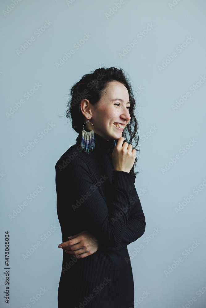 A stunning portrait of a beautiful woman with curly hair, a chic black turtleneck, elegant earrings, joyfully smiling against a clean, minimalist background that enhances her charm