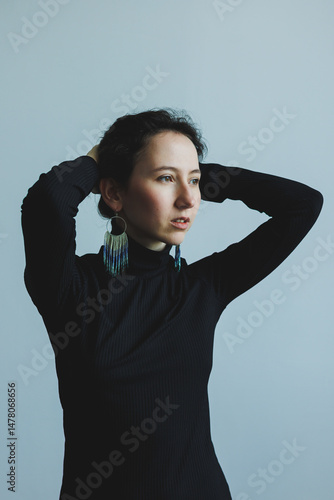 This captivating portrait shows a confident woman in a sleek black turtleneck, accentuated by bold earrings, with a minimalist background that highlights her elegance and sophistication
