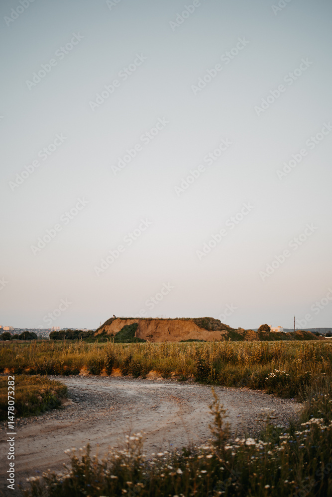 A breathtakingly serene rural landscape is observed at dusk, showcasing rolling hills alongside a gently winding gravel path that invites exploration through the tranquil countryside