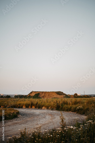 A breathtakingly serene rural landscape is observed at dusk, showcasing rolling hills alongside a gently winding gravel path that invites exploration through the tranquil countryside