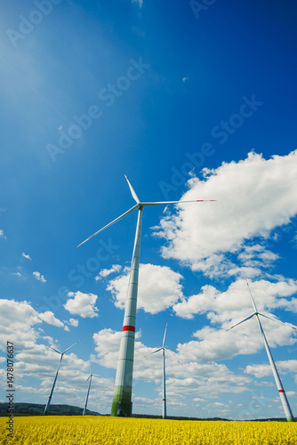 Obraz na płótnie Tall, vibrant wind turbines rise against a stunning blue sky with fluffy clouds, surrounded by golden fields. This scene symbolizes renewable energy and sustainable development in our modern world w salonie