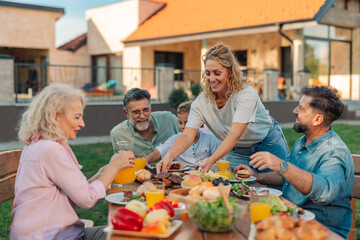 Happy family enjoying backyard barbecue, serving food and beverages on sunny day