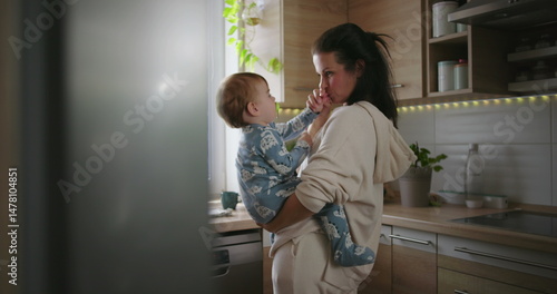 Mother smiling at baby in kitchen, casual parenting and bonding moment during warm family morning routine, home life with nurturing and love