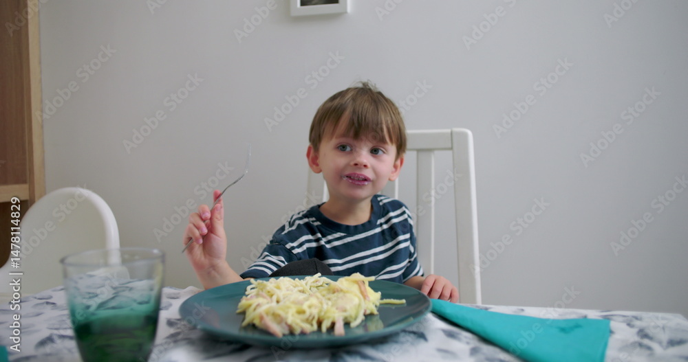 Young boy sitting at dining table enjoying pasta meal, holding fork, smiling, relaxed and happy, intimate family dining moment in cozy home environment Young boy sitting at dining table enjoying pasta meal, holding fork, smiling, relaxed and happy, intimate family dining moment in cozy home environment