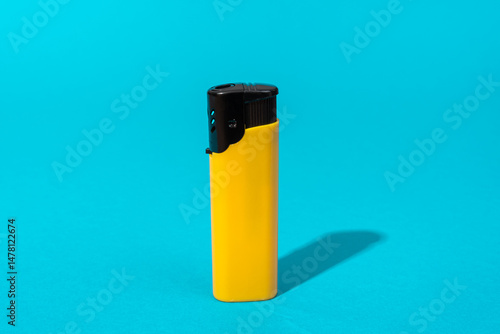 Minimalist photo of yellow disposable plastic lighter on turquoise blue background.