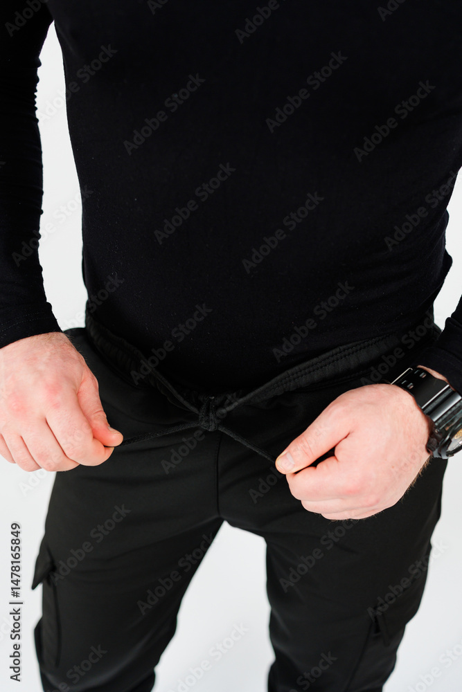 A person is seen adjusting the waistband of their black cargo pants while wearing a laidback outfit. This image captures various aspects of apparel, fashion, style, and everyday lifestyle