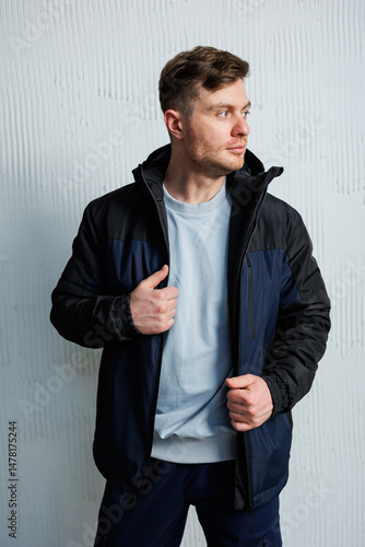 A confident male model in stylish outdoor attire poses against a textured backdrop, enhancing the visuals and making him the focus of a fashionable photoshoot that showcases his allure