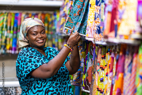 Smiling African woman, successful small business owner of an African Print, Ankara fabric shop proudly displaying textiles prints.