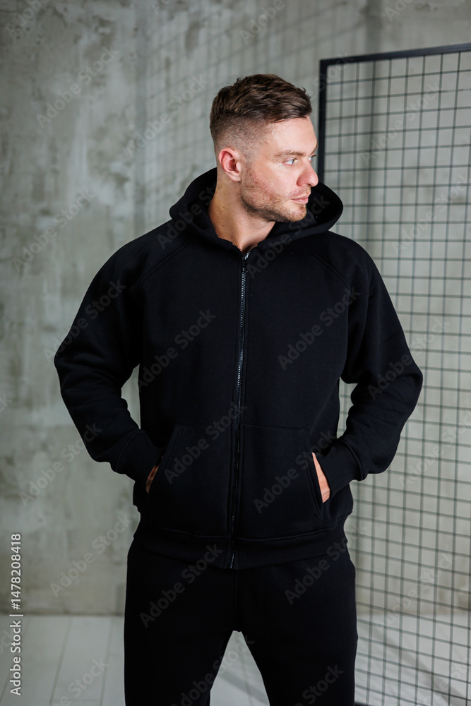 In 2023, delve into the latest fashion trends that highlight the growing presence of sportswear in everyday wardrobes. This style is exemplified by a fashionable man sporting a sleek black hoodie
