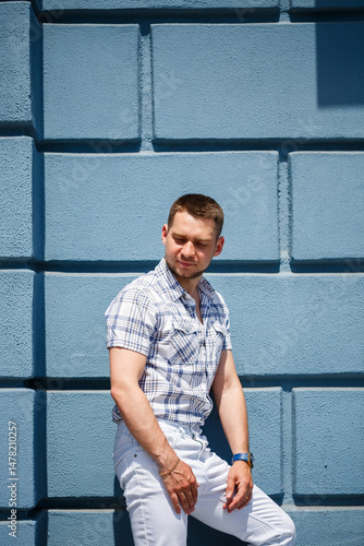 A Stylish Man Posing Confidently Against a Bright Blue Wall, Showcasing a Fashionable Summer Outfit That Perfectly Blends Unique and Colorful Accessories with Modern Design Elements for a Trendy Look