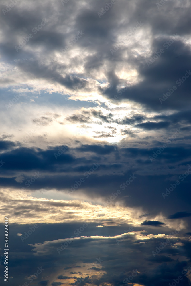 Fototapeta premium Scenic sunset with dramatic cloud formations painted in shades of orange, yellow, and deep blue. The play of light and shadow creates a mesmerizing natural composition.