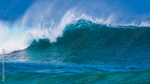 Fotografie Offshore wind grooms beautifully a smooth breaking ocean wave that curls under clear blue skies
