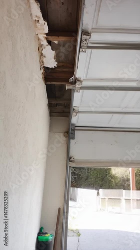 Damaged garage wall reveals wooden frame, creating a hole exposing the ceiling, highlighting home repair needs and structural issues