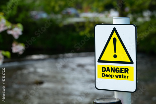 Danger Deep Water sign in front of a river with a weir in the background. 