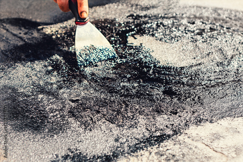 Tableau sur toile Person using a putty knife to spread a thick, black tar substance across a rough surface,  for roof repair