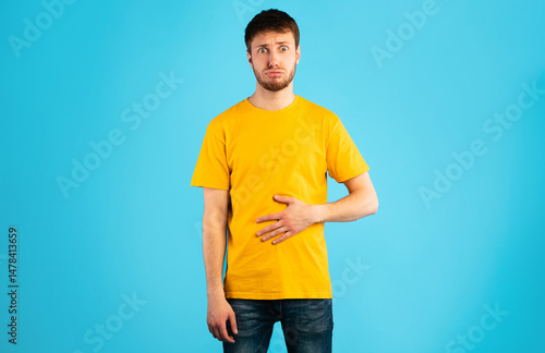 Young male model touching his stomach, feeling satiety after eating hearty meal, having good appetite