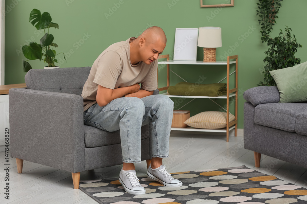 Fototapeta premium Young man with appendicitis sitting in armchair at home