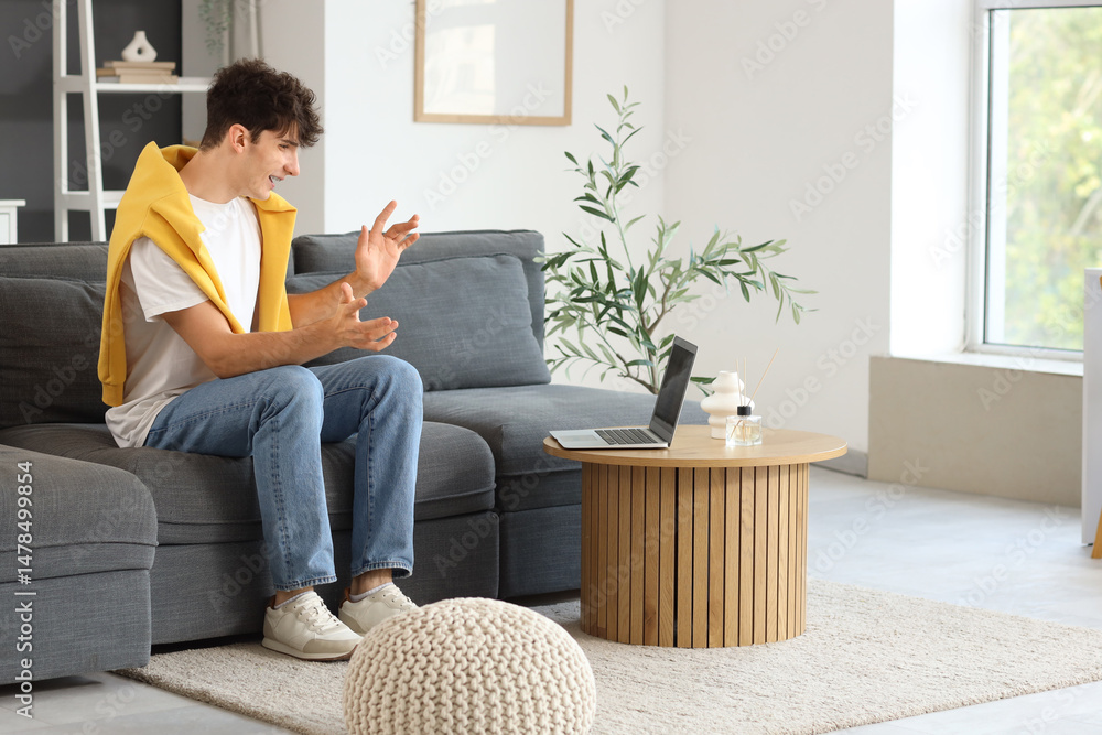 Obraz premium Young man video chatting with laptop on sofa at home