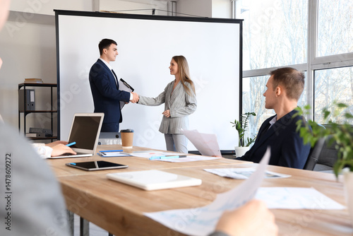 Business partners shaking hands near projector screen in conference room