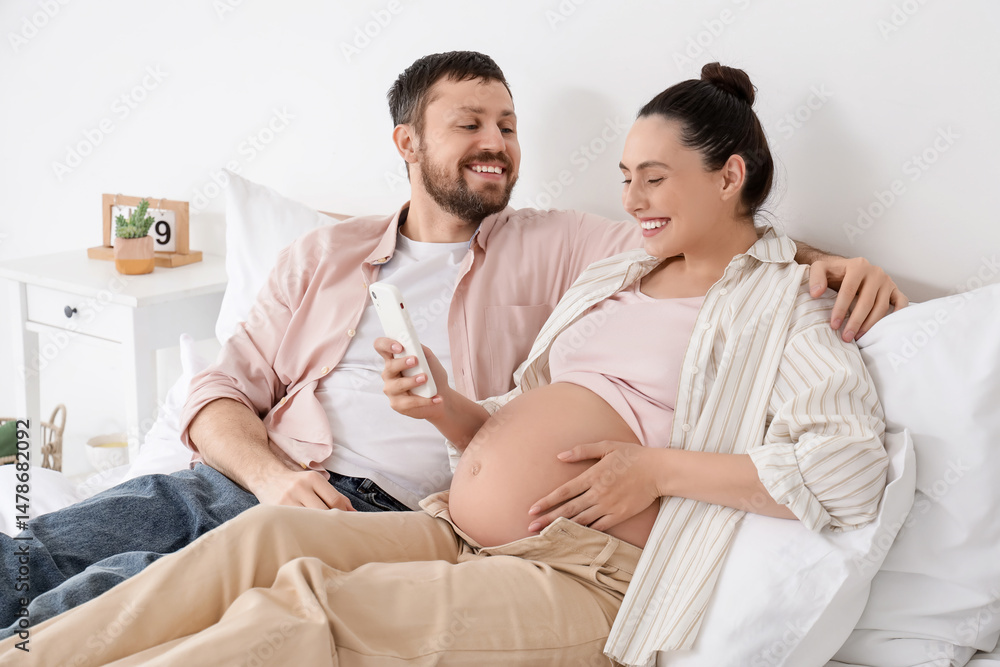 Happy pregnant couple using mobile phone in bedroom Happy pregnant couple using mobile phone in bedroom