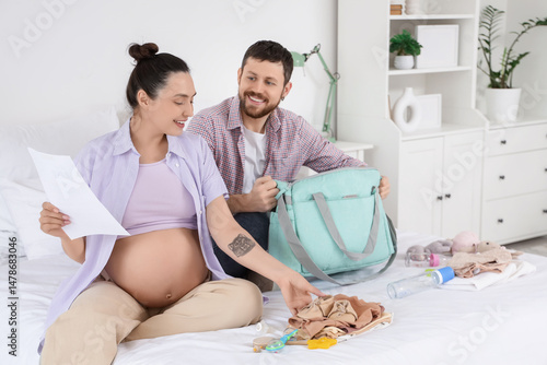 Happy pregnant couple with checklist packing maternal hospital bag in bedroom