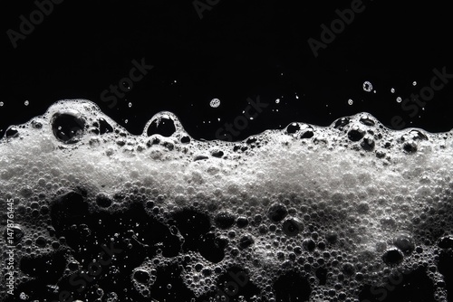 Close-up view of sudsy bubbles on a black background.  A frothy layer of white bubbles crests over a dark surface.  Bubbles vary in size and shape, creating a textured surface