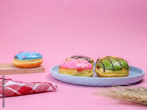 Colorful assorted donuts with icing and sprinkles on pastel pink background