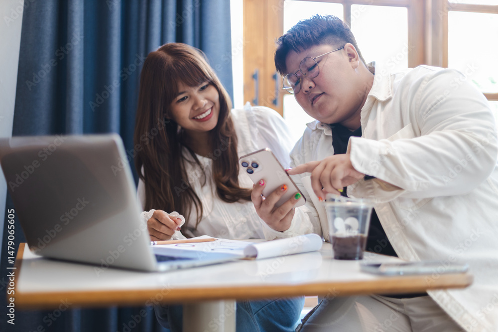 Diverse couple of gender fluid individuals enjoy relaxed lifestyle together while using smartphone in cozy indoor setting with laptop and notes Diverse couple of gender fluid individuals enjoy relaxed lifestyle together while using smartphone in cozy indoor setting with laptop and notes