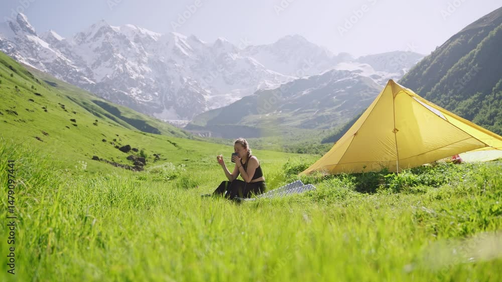 custom made wallpaper toronto digitalWoman enjoys breakfast, drinks coffee on outdoor backpacking trip with yellow tent. Scenic mountain landscape, green meadow. Solo traveler in nature, adventure seeker, camping, morning relaxation.
