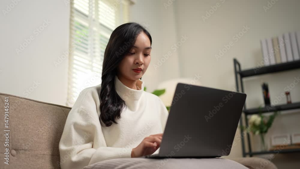 Focused asian woman working remotely from her comfortable living room Focused asian woman working remotely from her comfortable living room