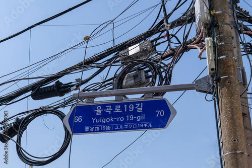 Close up of street sign in Seoul, South Korea on 19th Street, Chesnut Road (translates in Korean Language and characters) with multiple electricity cables hanging above from concrete pole